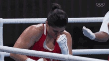 a woman in a red tank top is in a boxing ring with the olympic rings visible in the background