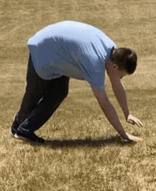 a man in a blue shirt is bending over in the grass on a field .