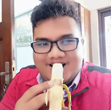 a man wearing glasses is eating a banana in front of a door