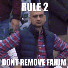 a man wearing a plaid shirt and a vest with rule 2 dont remove fahim written on it