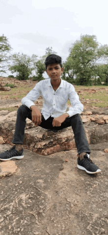 a young man is sitting on a rock wearing a white shirt and black pants .