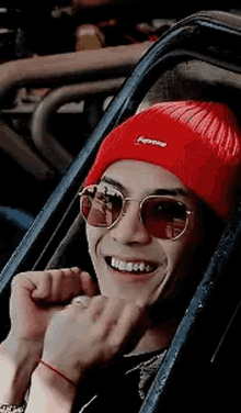 a young man wearing a red beanie and sunglasses is sitting in a car .