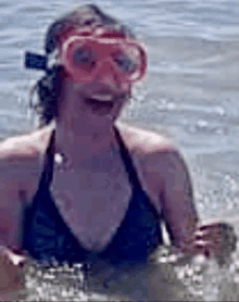 a woman in a bikini is swimming in the ocean wearing a pink mask .