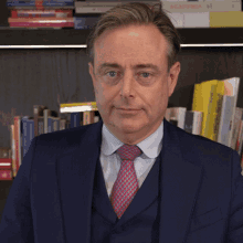 a man in a suit and tie is standing in front of a bookshelf with a book titled aca mia on it