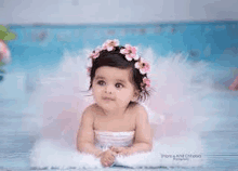 a baby girl wearing a flower crown and a tutu is laying on a blue blanket .