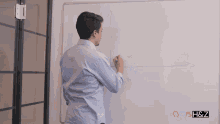 a man is writing on a whiteboard with a h & z logo in the background