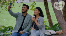 a man is taking a selfie with a woman while they sit under a tree with a hello again sign behind them