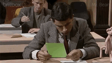 a man in a suit and tie is sitting at a desk looking at a piece of paper with a britbox logo behind him