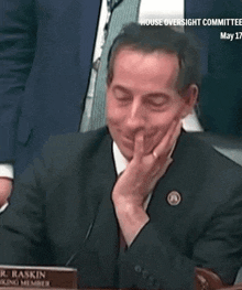 a man in a suit and tie sits at a table with a name plate that says " r.j. raskin "