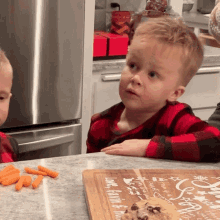 two young boys are sitting at a counter with a cutting board that says love faith and family on it