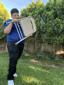 a boy in a blue shirt is holding a folding chair over his head