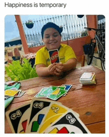 a boy in a yellow shirt is playing uno cards at a table