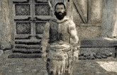 a man with a beard and a sword is standing in front of a wooden building .