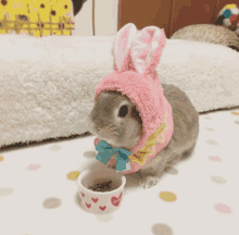 a small rabbit wearing a pink bunny hat is eating out of a bowl