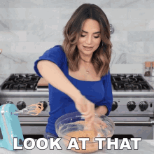 a woman in a blue shirt is mixing something in a bowl with the words look at that above her