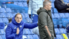 two men are standing next to each other in a stadium during a soccer match .