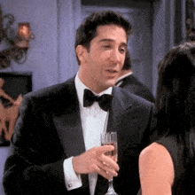 a man in a tuxedo is holding a glass of champagne next to a woman .