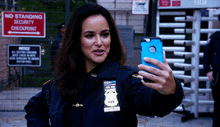 a woman in a police uniform is taking a selfie with her cell phone in front of a no standing security checkpoint sign