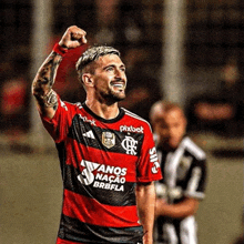 a soccer player is raising his fist in the air while wearing a red and black uniform .