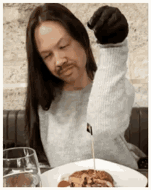 a woman with long hair and a fake mustache is sitting at a table with a plate of food and a glass of water