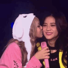 two girls are kissing each other on the cheek while holding microphones .