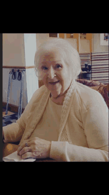 an elderly woman in a tan sweater is smiling at the camera