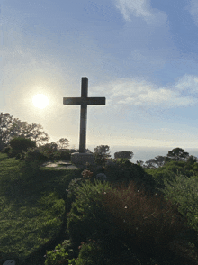 a cross on top of a grassy hill with the sun shining through the clouds