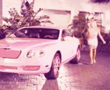 a woman walking past a pink car on a brick road