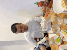 a man sitting at a table with a bottle of sriracha sauce