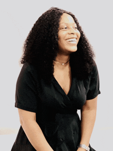 a woman with curly hair wearing a black dress smiles