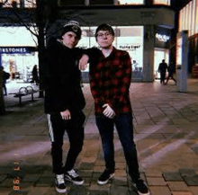 two young men standing next to each other on a sidewalk .