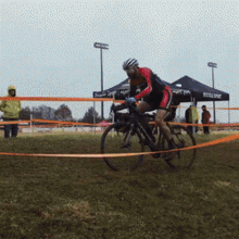 a person riding a bike in a field with a tent that says ' altitude ' on it in the background