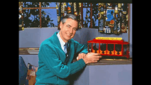 a man in a blue sweater is holding a toy trolley that says neighborhood trolley