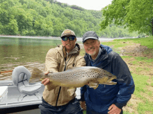 two men are holding a large brown trout in front of a boat