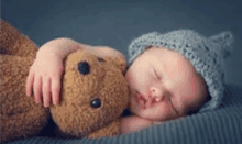 a newborn baby is sleeping with a teddy bear .