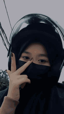 a woman wearing a black mask and a helmet giving the peace sign