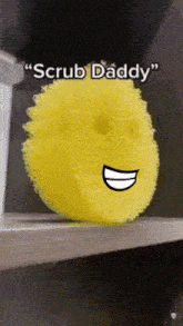 a yellow sponge with a smiling face and the words " scrub daddy " below it