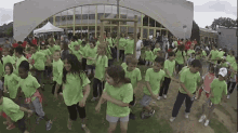 a group of children wearing green shirts with the letter c on them are dancing in front of a building