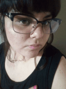 a woman wearing glasses and a black tank top has a piercing in her nose