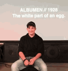 a young man is sitting in front of a projector screen that says albums / 1928 the white part of an egg