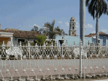 a white wrought iron fence surrounds a street with a church tower in the background