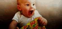 a baby is sitting on a couch with his mouth open and holding a piece of birthday wrapping paper .