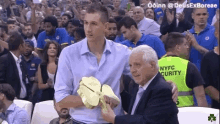 a man in a blue shirt is holding a trophy in front of a crowd with nyfc security in the background