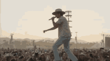 a man in a hat singing into a microphone in front of a crowd at a stage which has the word stage on it