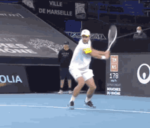 a man swings a tennis racquet on a tennis court in front of a sign that says " ville de marseille "