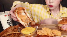 a woman in a yellow plaid shirt is eating a kfc meal