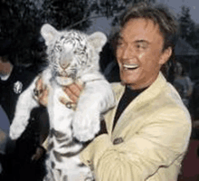 a man in a suit is holding a white tiger cub on his shoulders .