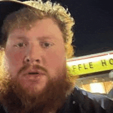 a man with a beard and a hat is standing in front of a sign that says affle house .