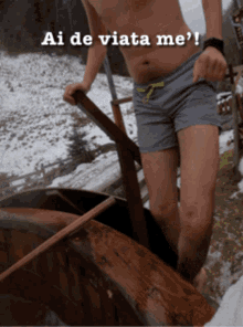 a shirtless man in shorts is standing next to a wooden boat with the words ai de viata me written above him