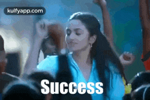 a woman in a blue shirt is dancing in front of a crowd and the word success is written above her .